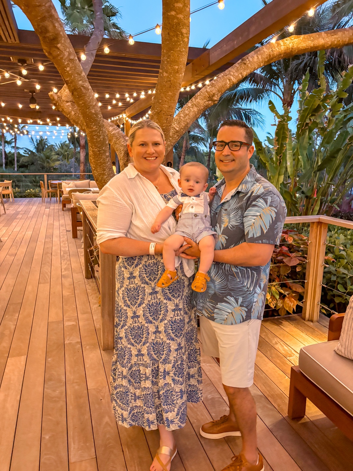 A family of three dressed for dinner on a tropical restaurant terrace at sunset
