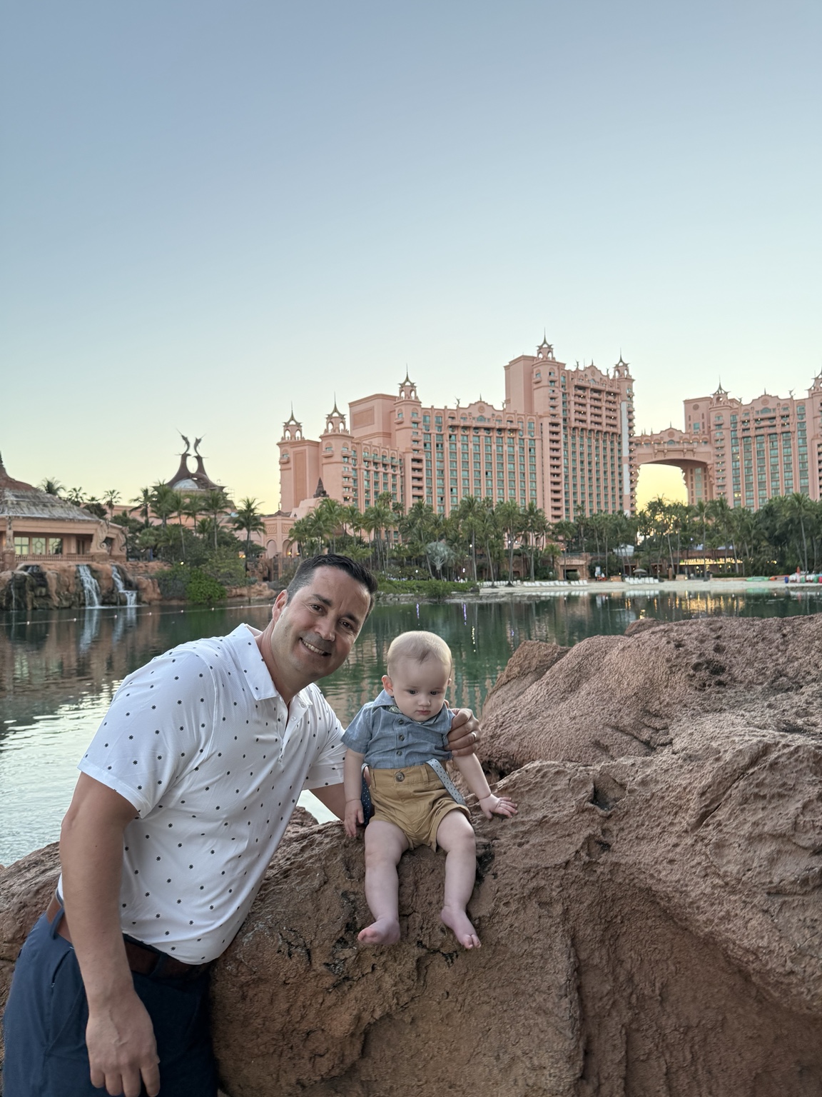 Hassan and his baby beside a lagoon with the iconic Atlantis towers in the background