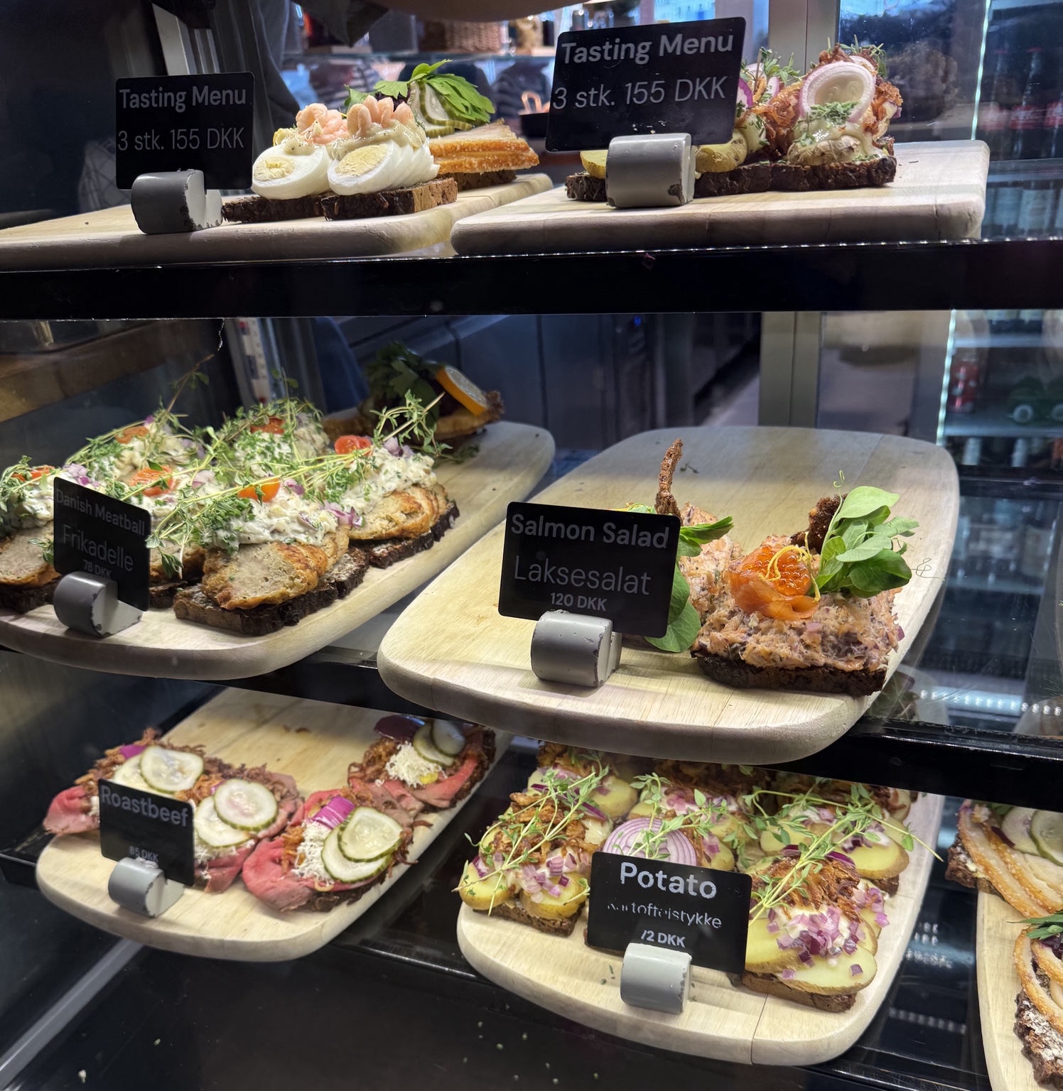 Rows of Danish open-faced sandwiches in the display case, topped with shrimp, eggs, meatballs, salmon, roast beef and potatoes