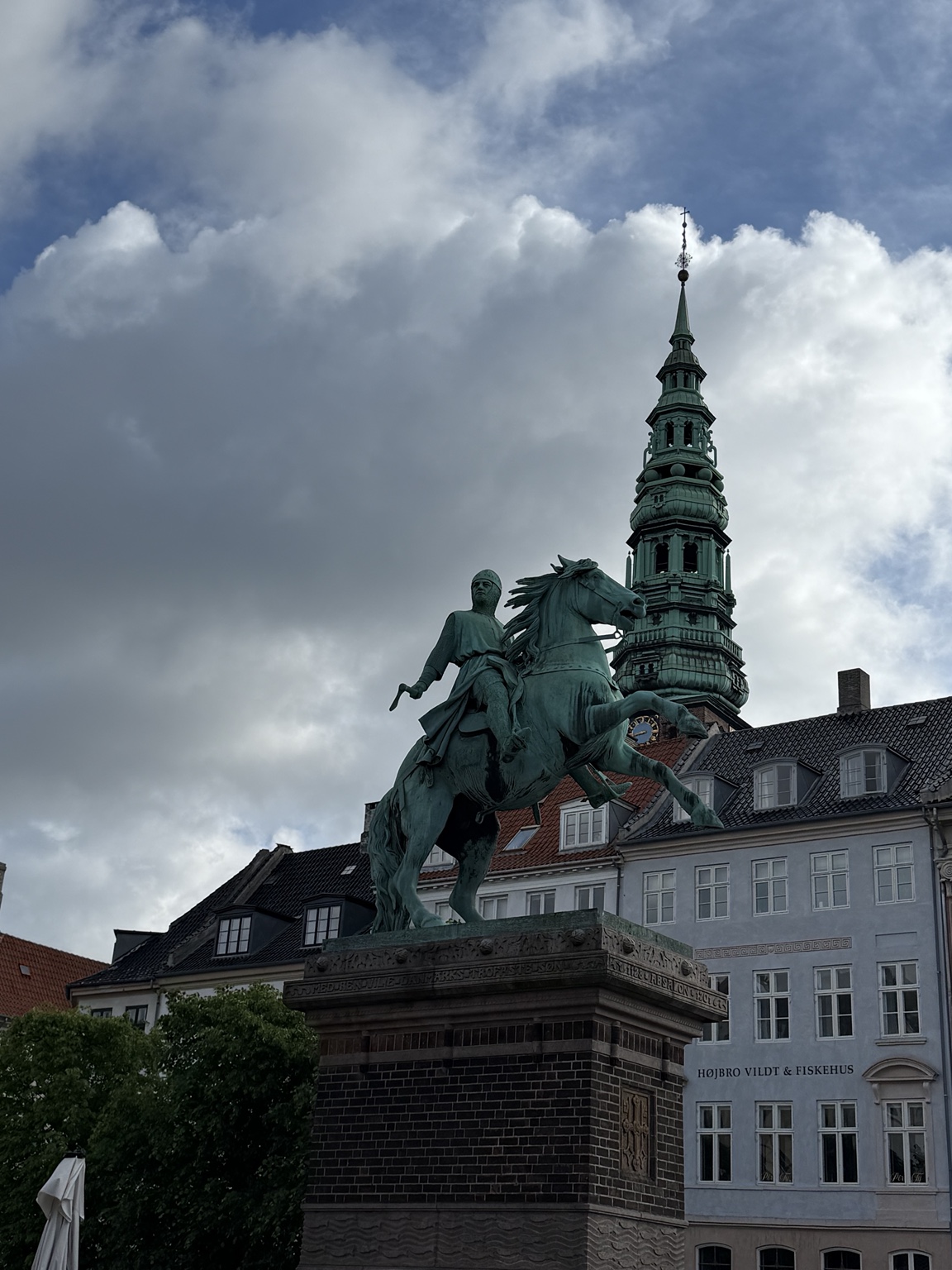 An equestrian statue with a green copper spire rising behind it in central Copenhagen
