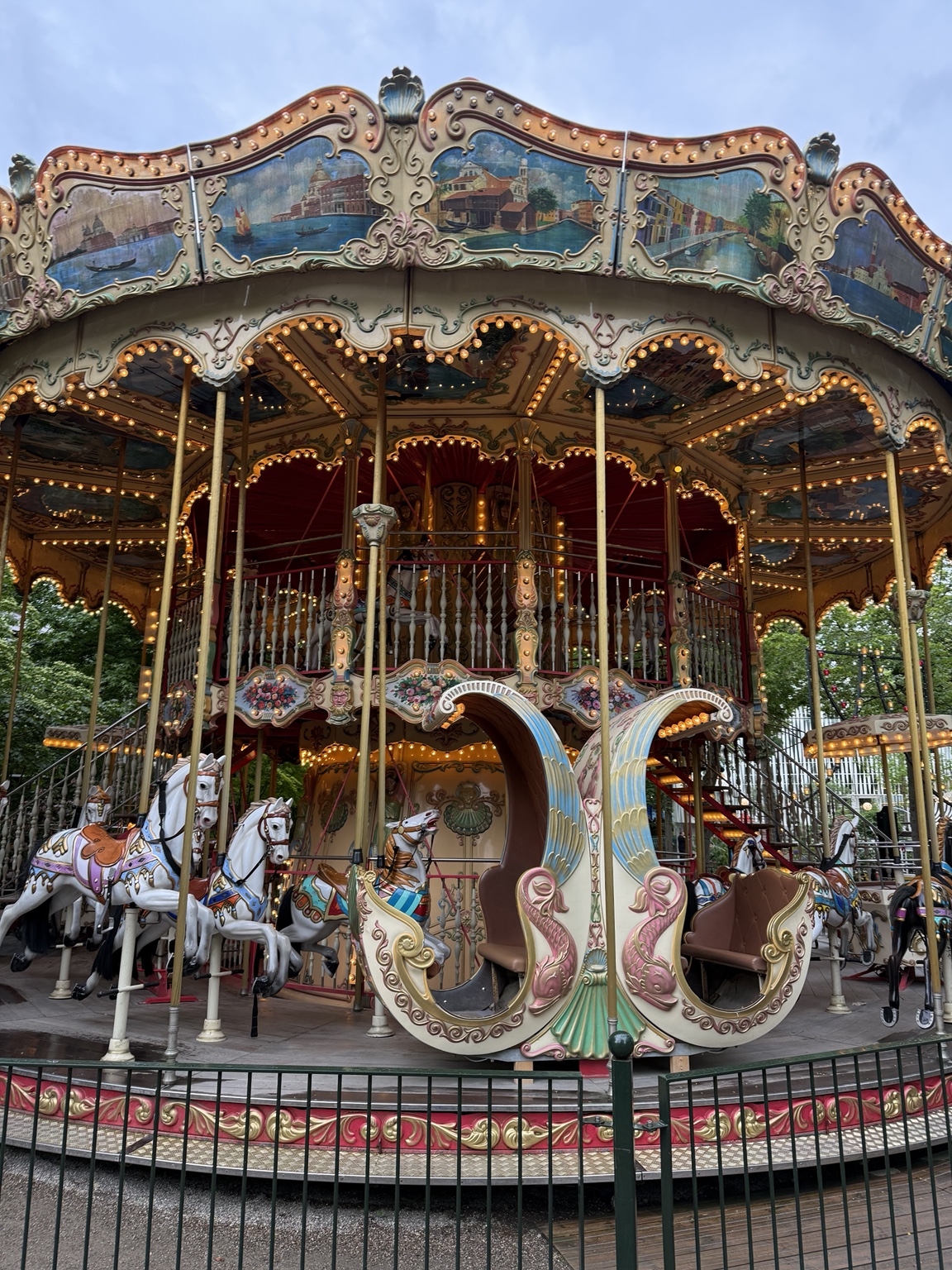 An ornate double-decker carousel with painted horses, a carriage and glowing lights at Tivoli