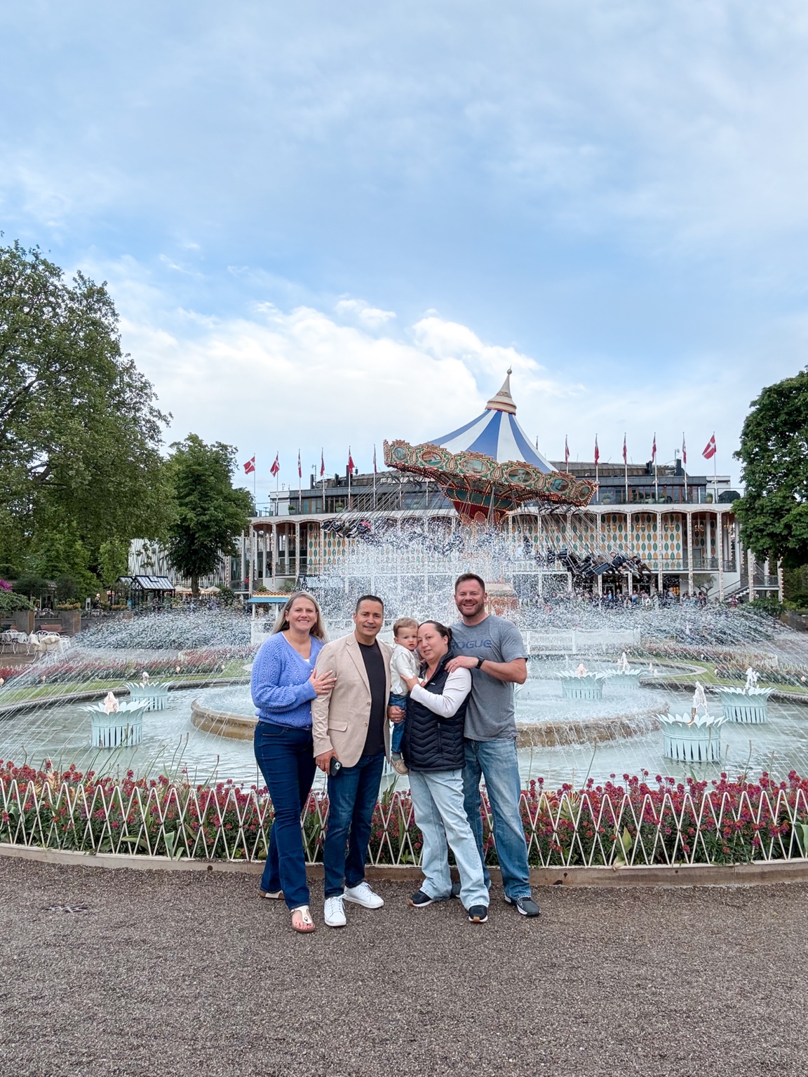 Family members and a toddler together in front of the fountain and swing carousel at Tivoli Gardens