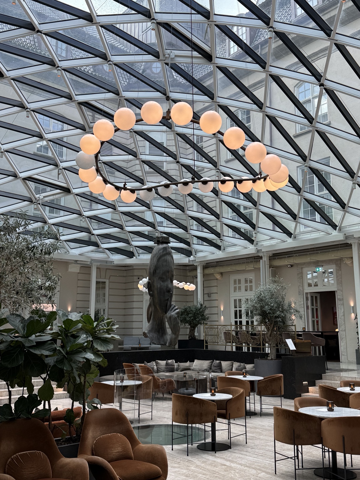 Villa Copenhagen’s glass-roofed courtyard with sculptural lighting, plants and lounge seating