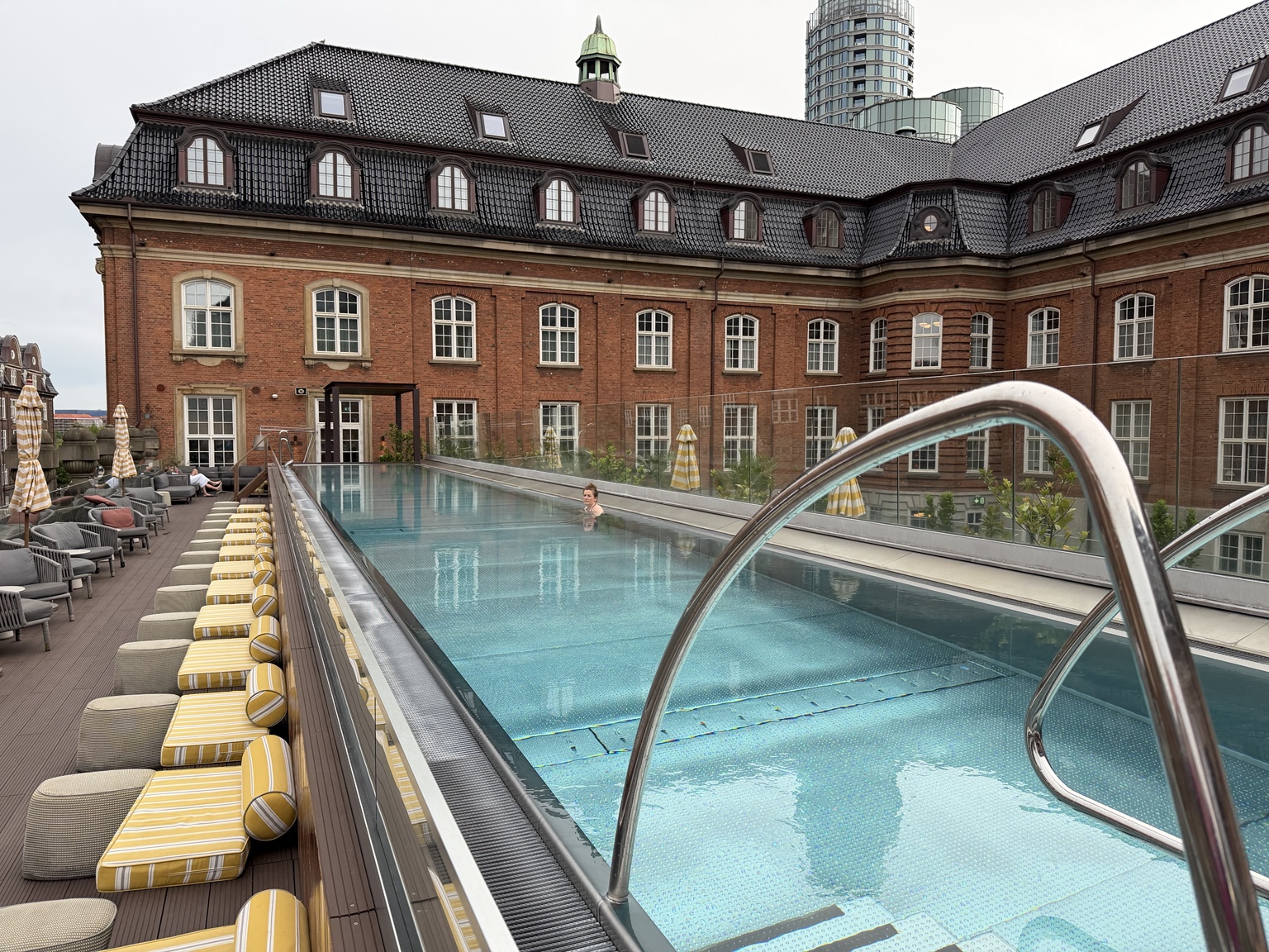 Villa Copenhagen’s outdoor lap pool beside striped yellow loungers and a red-brick building