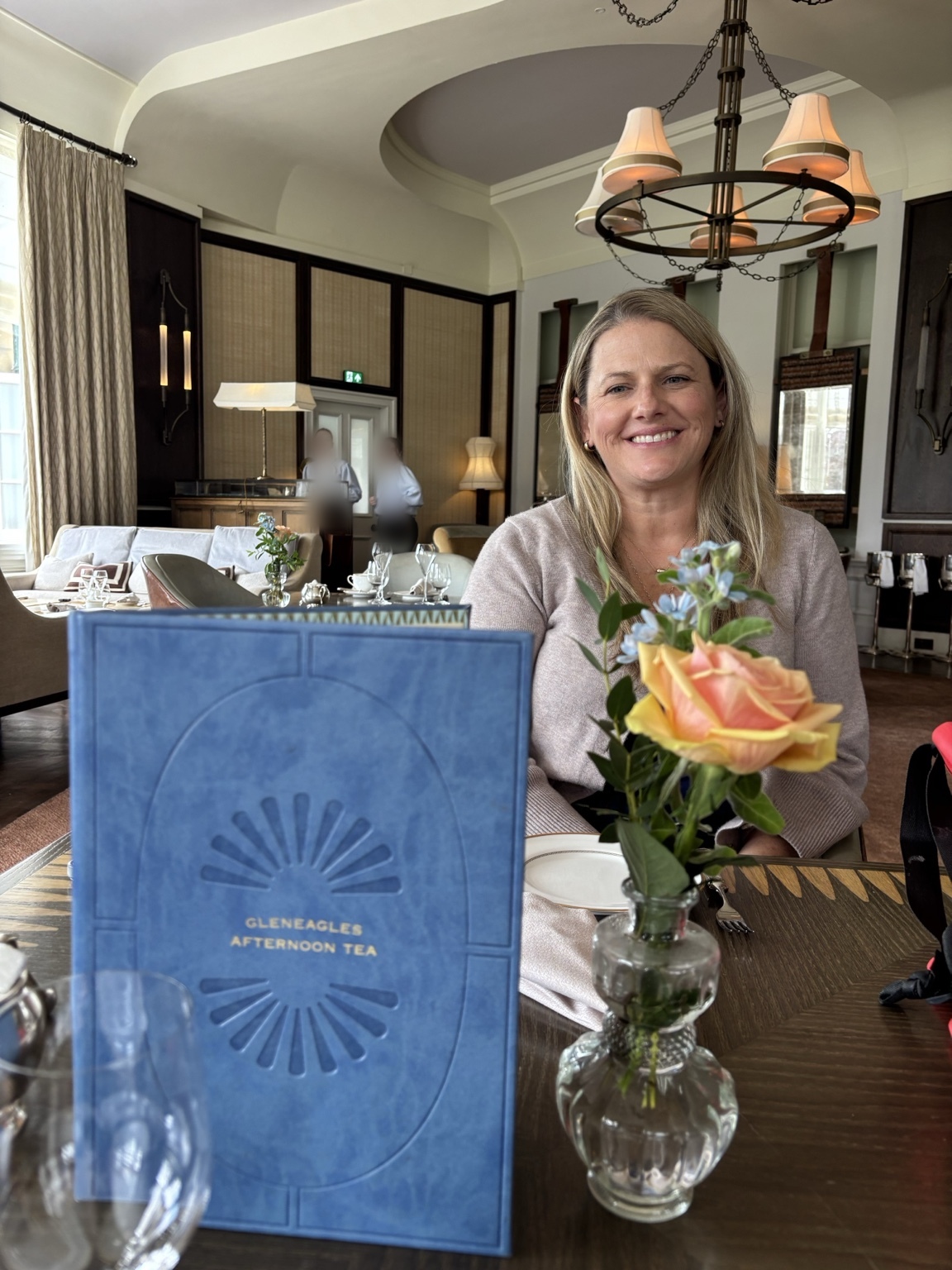 Jeni enjoying afternoon tea at Gleneagles beside flowers and the tea menu