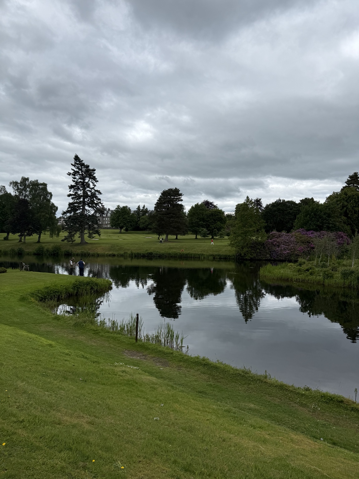 A calm lake, golf course and distant Gleneagles Hotel under a dramatic sky