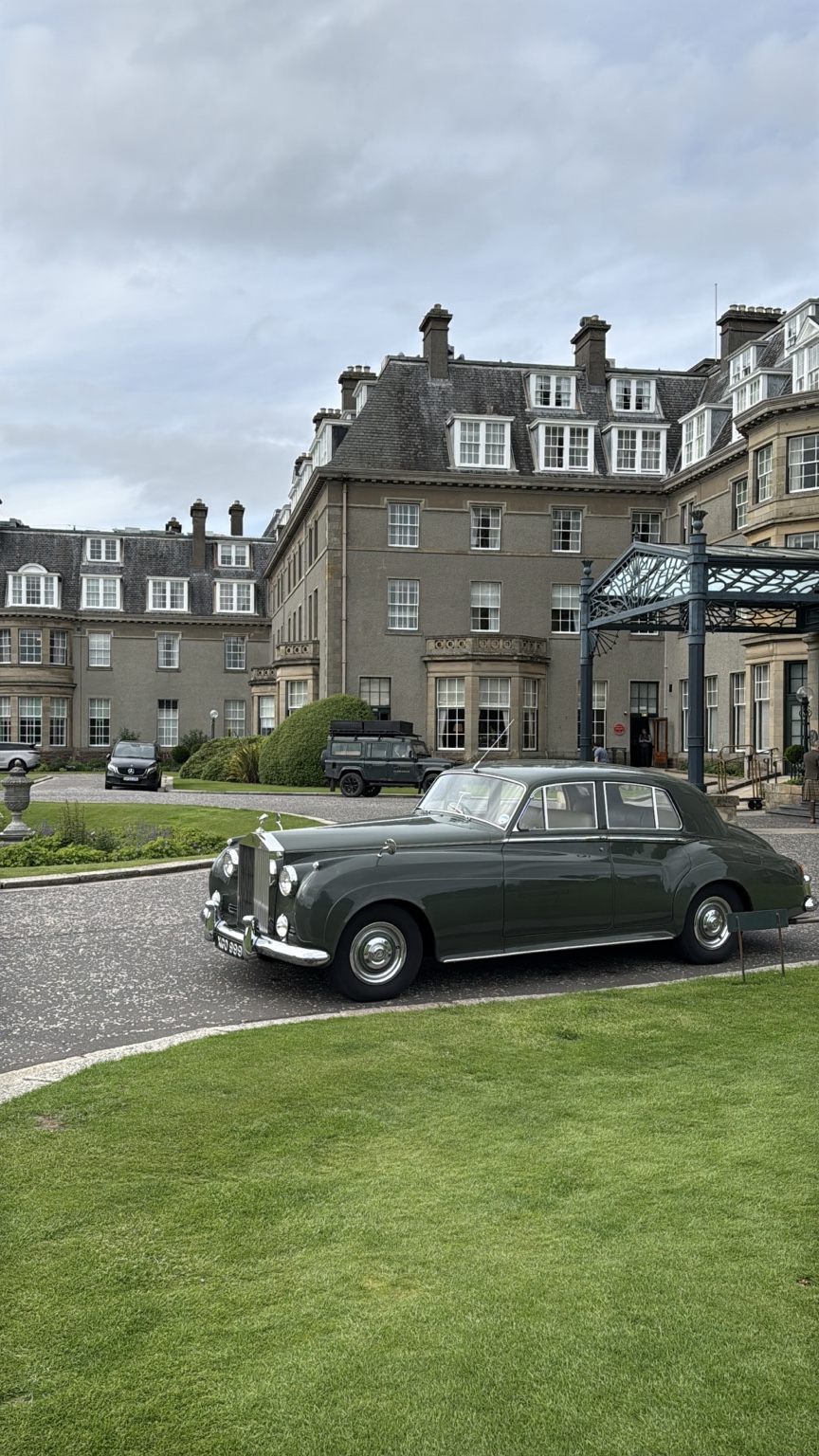 A vintage dark green car parked in front of Gleneagles Hotel