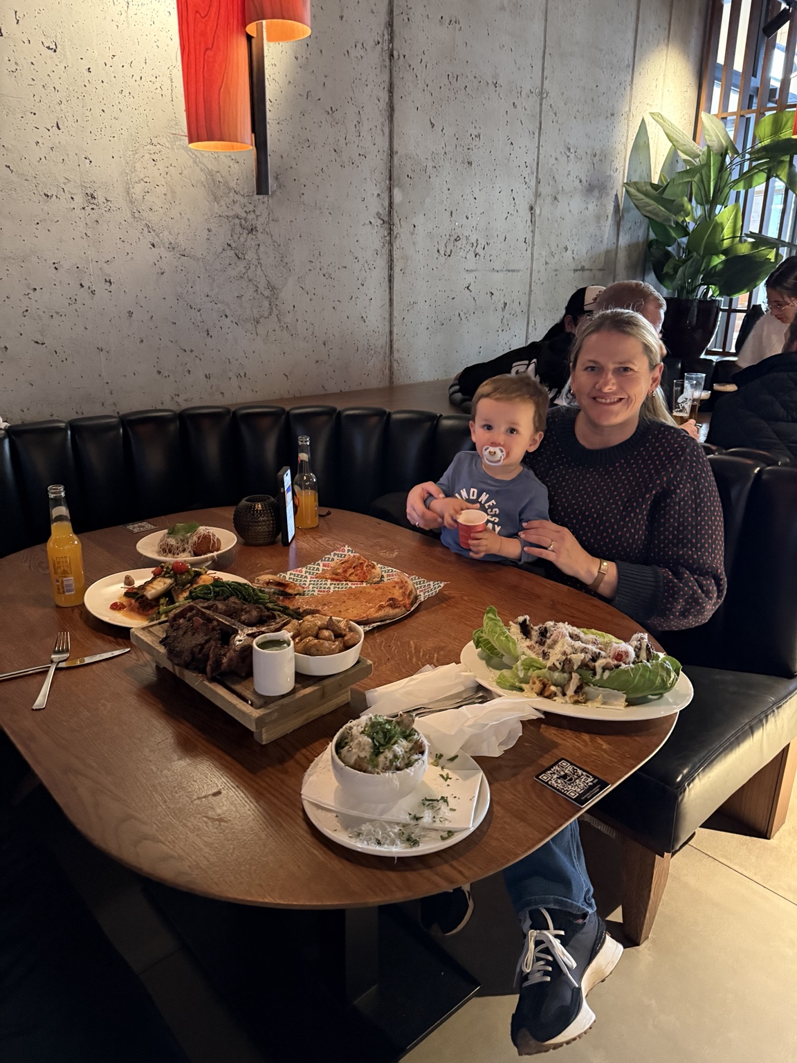 Jeni and her toddler at a table filled with steak, pizza and other dishes at Hafnartorg