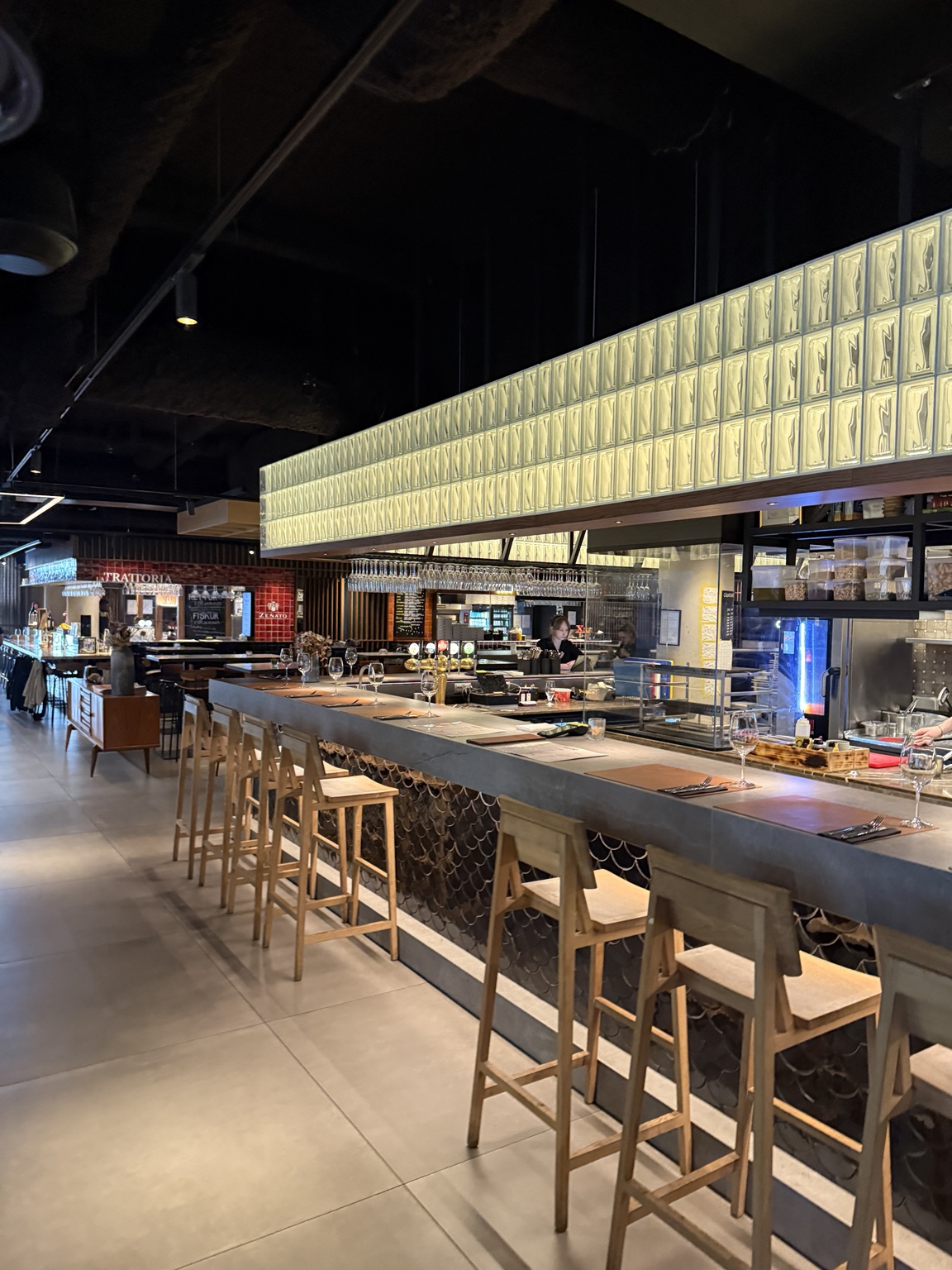 A long dining counter with wooden stools and illuminated glass blocks at Hafnartorg