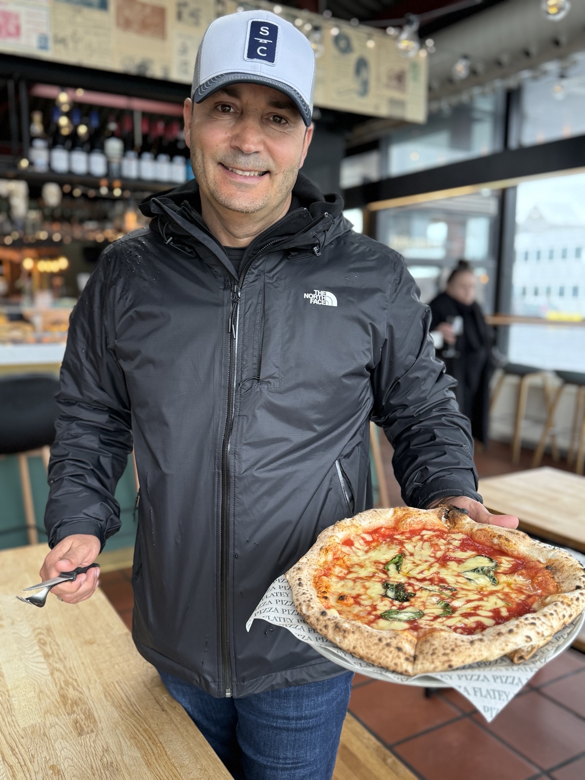 Hassan holding a tomato, cheese and basil pizza from Flatey at Hlemmur