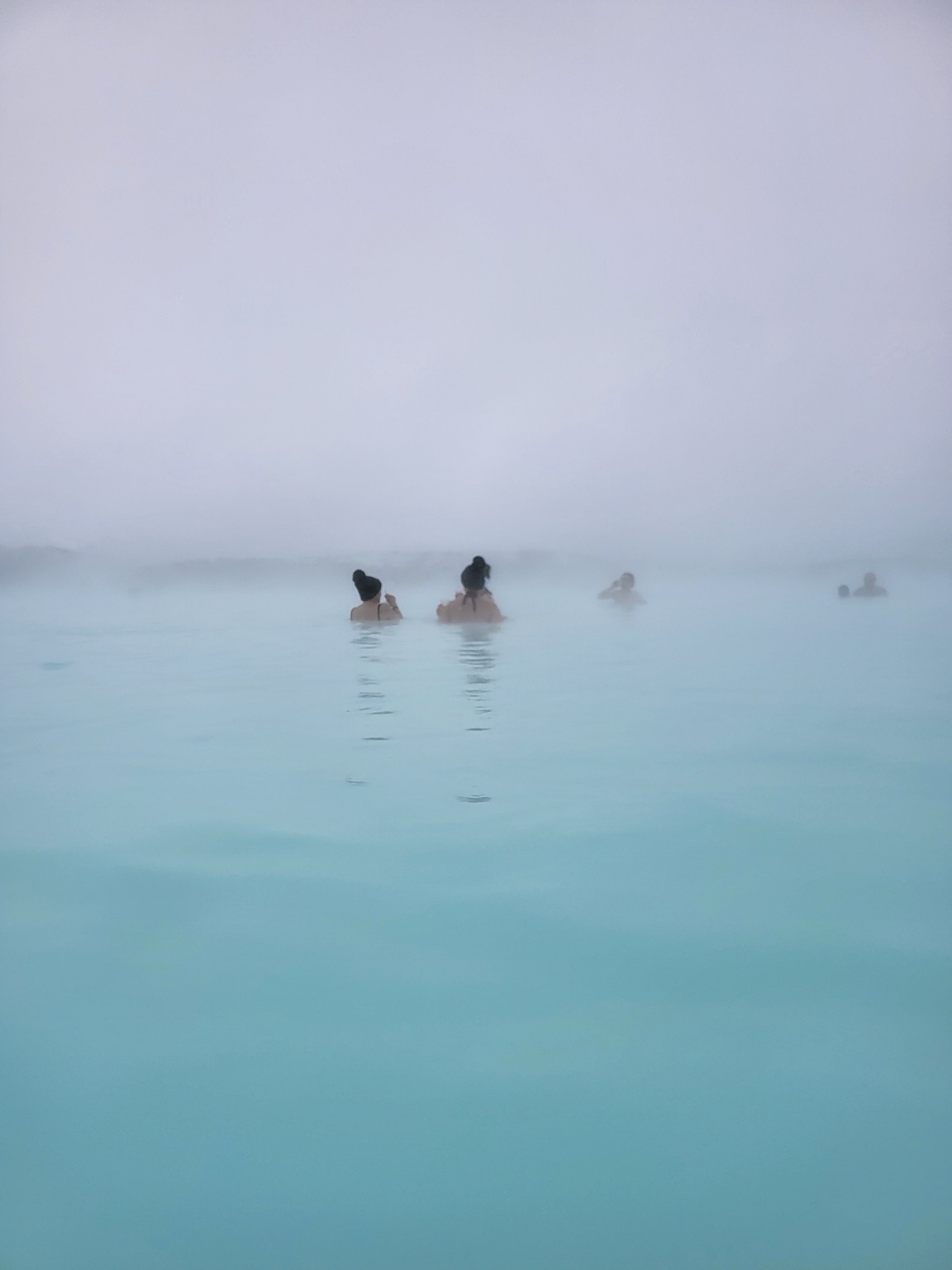 Bathers disappearing into mist across the pale blue water at Blue Lagoon