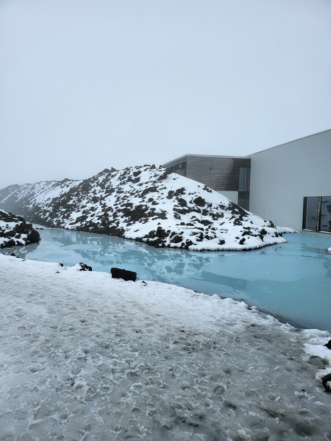 Pale blue geothermal water winding through snow-covered black lava at Blue Lagoon in Iceland