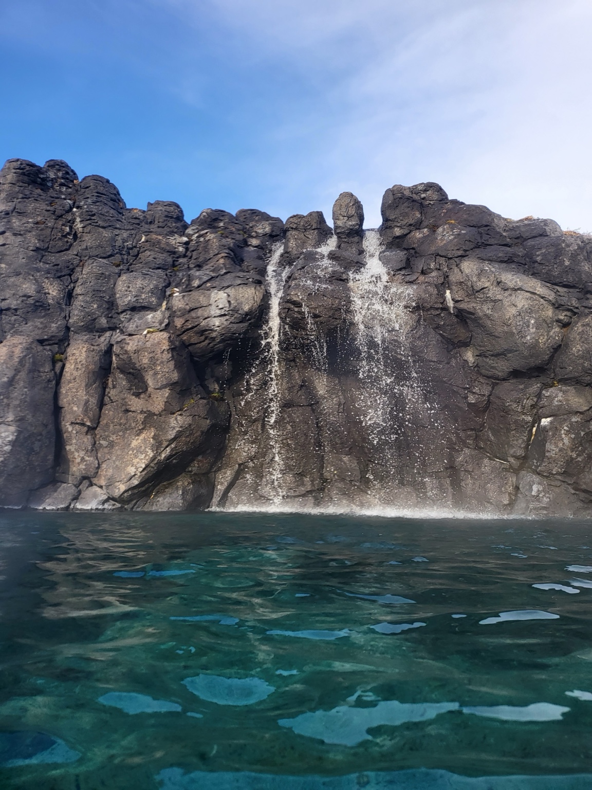 Water cascading over a dark rock wall into Sky Lagoon