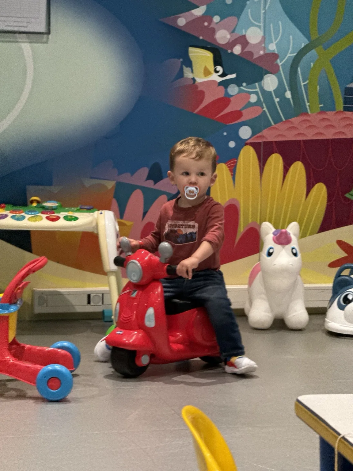 Our toddler riding a red toy scooter in the onboard Baby Club
