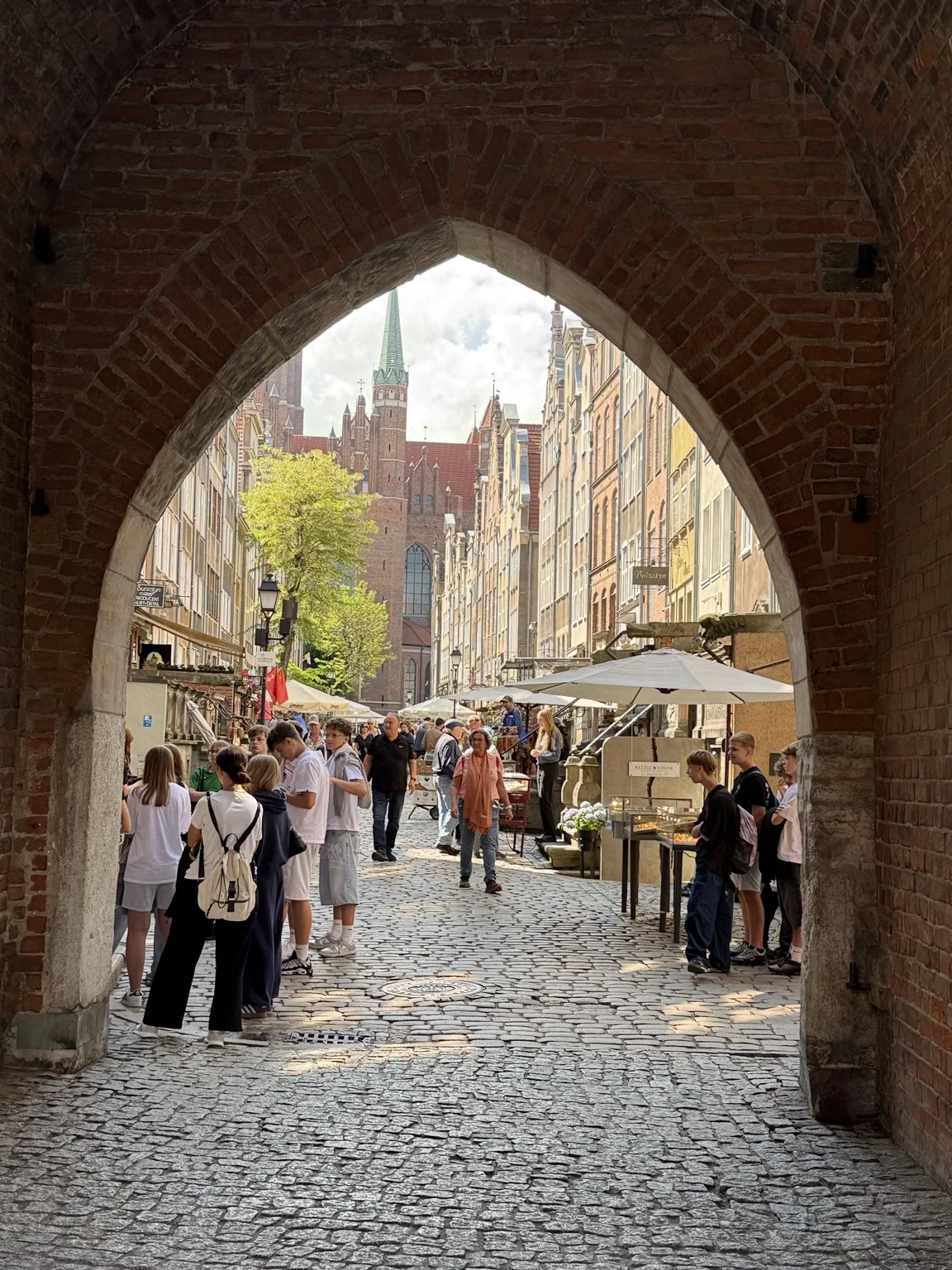 An arched brick gateway framing a cobbled street in Gdańsk