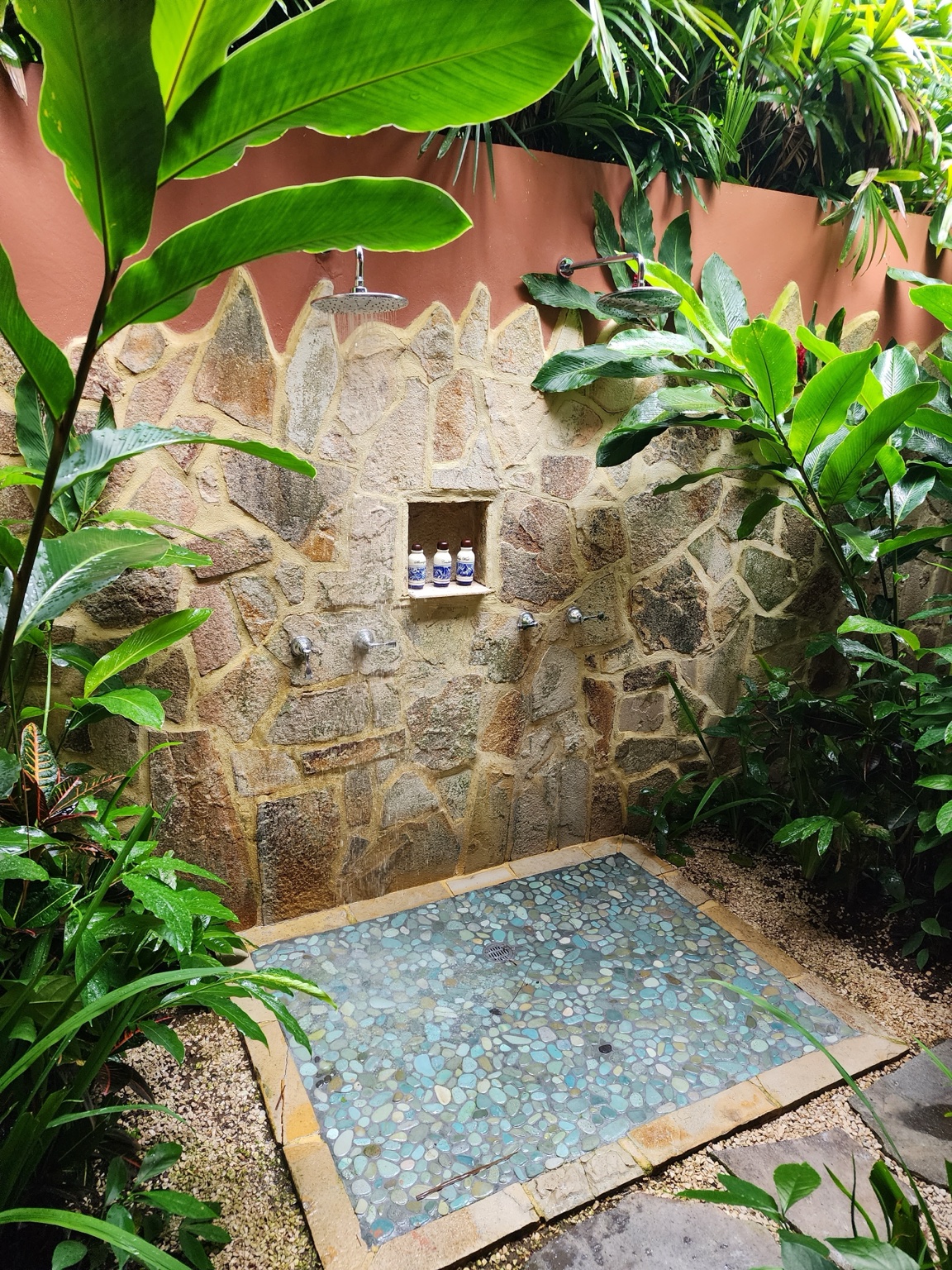 Two outdoor rainfall showers set against a stone wall and surrounded by tropical plants at Nayara Gardens
