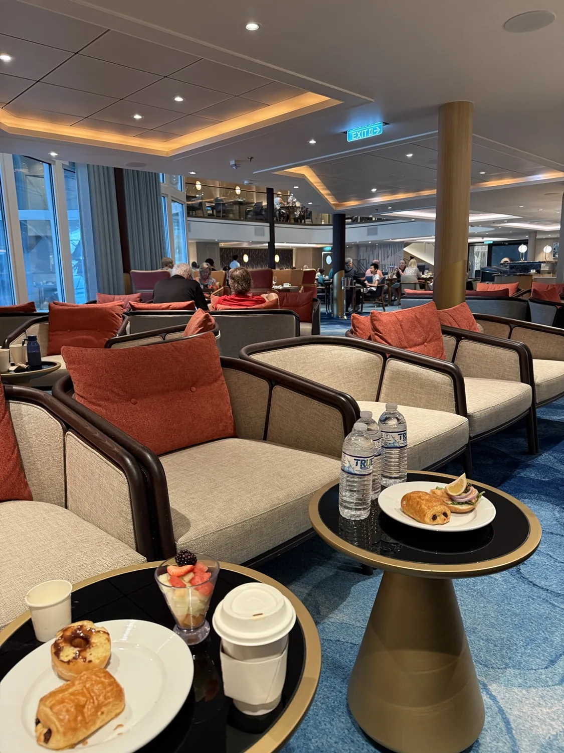 Cushioned chairs and tables in the Coastal Kitchen lounge area, with coffee and pastries in the foreground