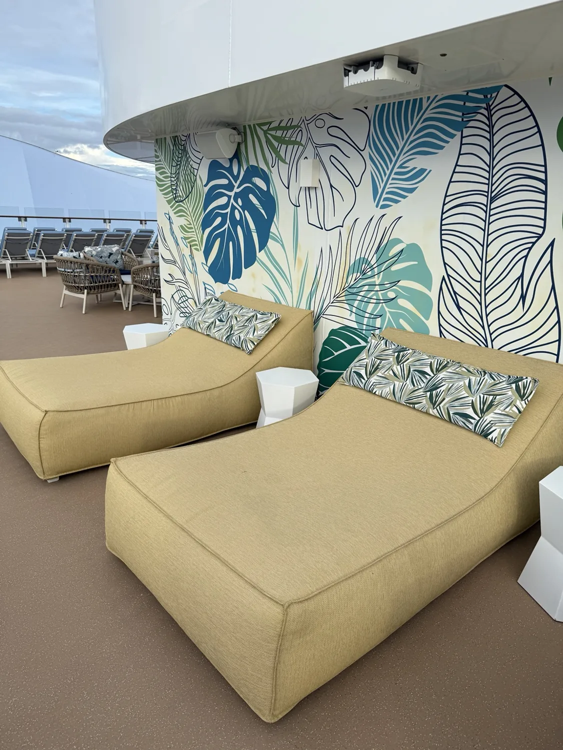 Large yellow daybeds with botanical cushions beside a leaf-patterned wall at The Grove