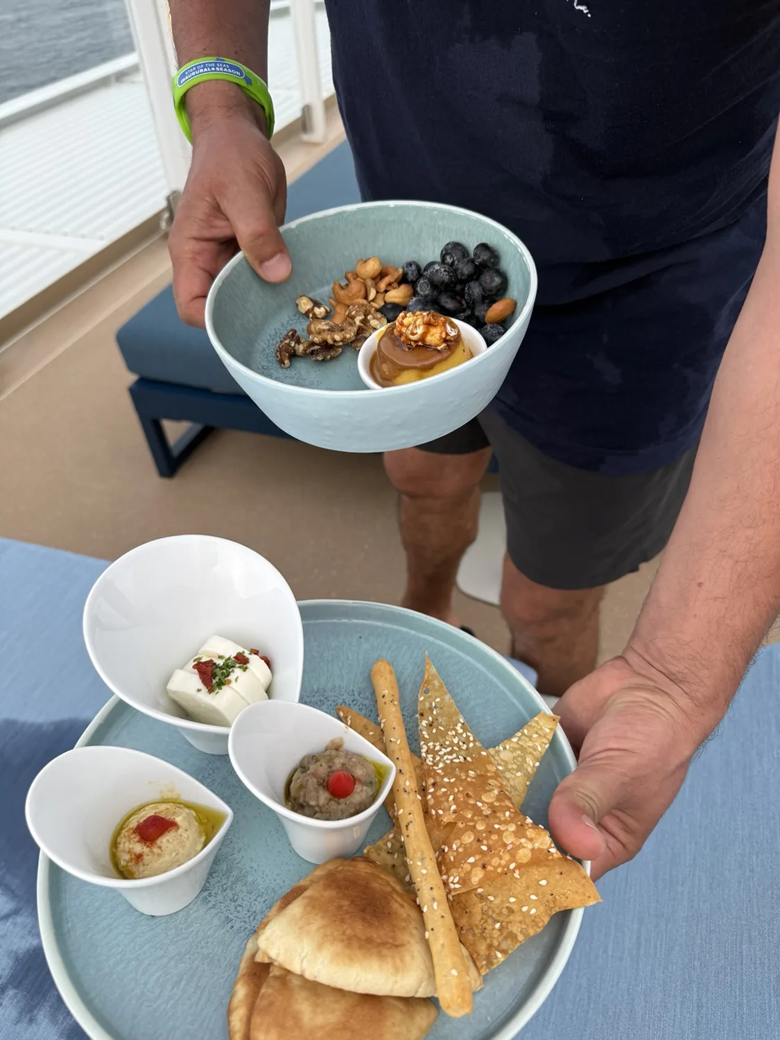 A plate of dips, breads and sesame crackers, with a bowl of fruit, nuts and a small dessert