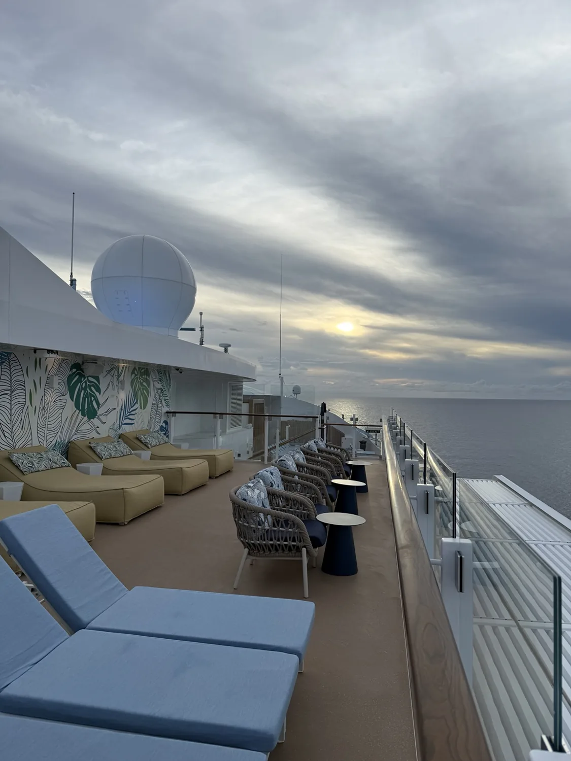 Ocean-facing cushioned chairs and blue loungers along The Grove’s sun deck at sunset